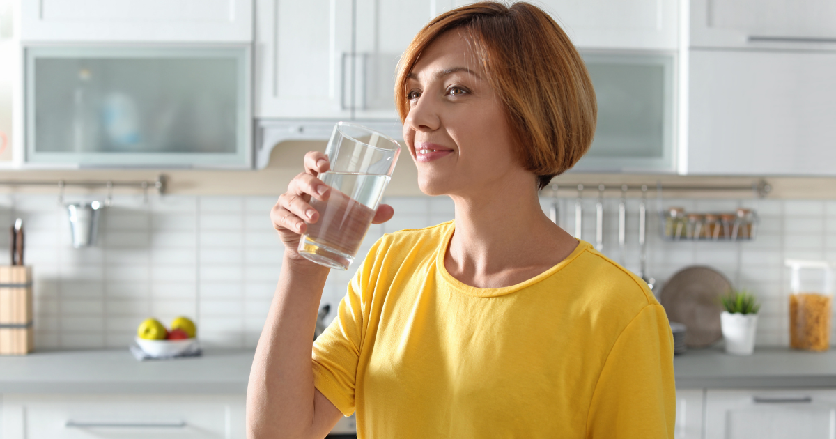 Water filtration systems are a valuable addition to any home, but how long does a whole house water filter system last? - happy woman drinking a glass of water in home kitchen